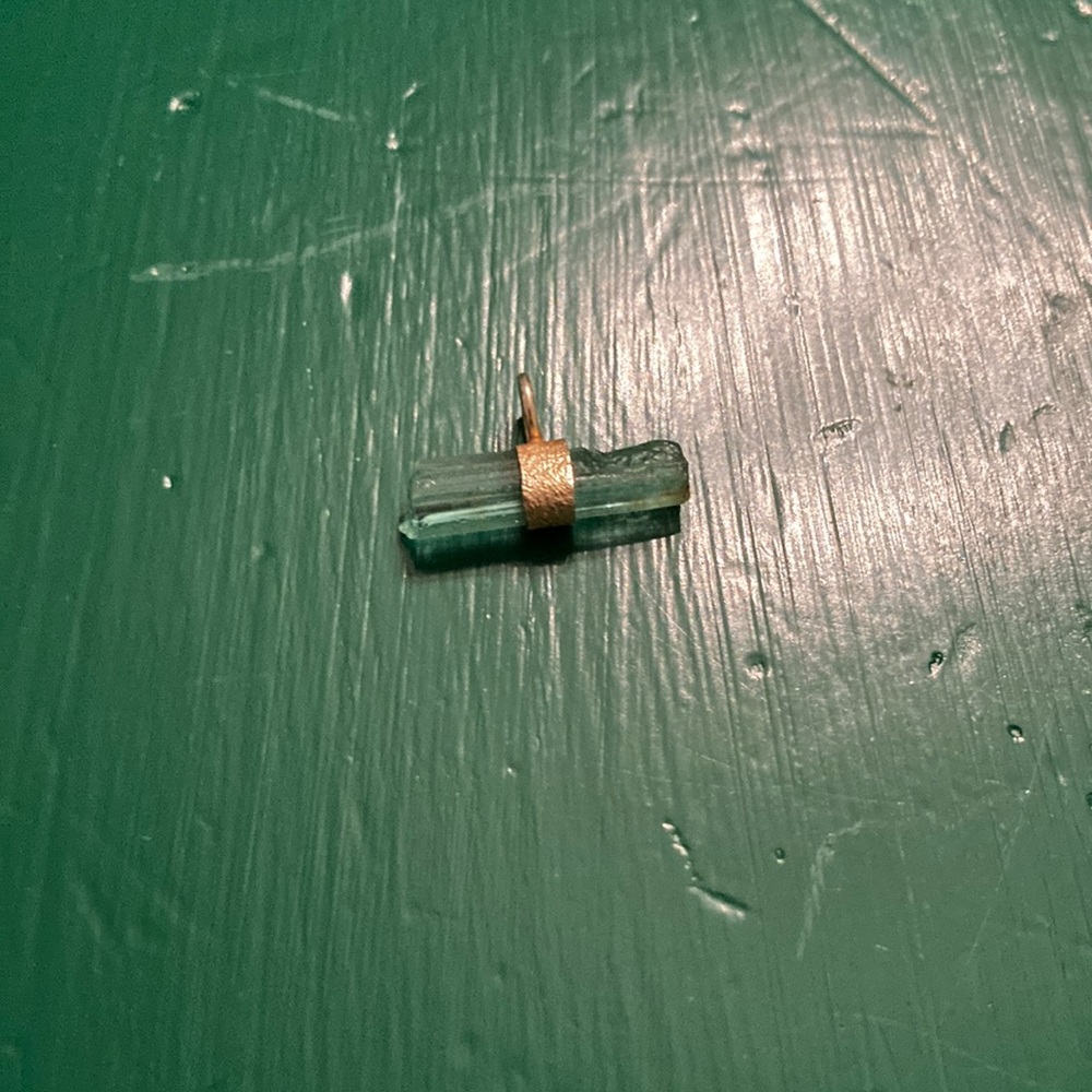 Unique raw aqua tourmaline set in gold coloured metal small bar pendant.